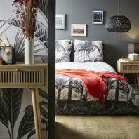 Lit parure blanche et palmiers noirs, dessus de lit orange, console en bois au premier plan